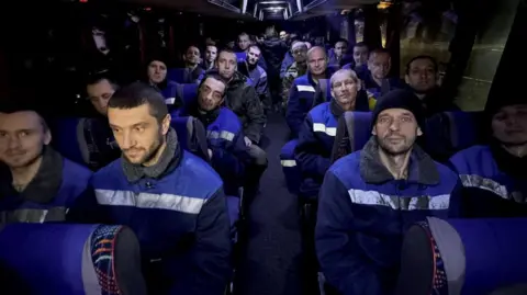 Zelenskiy/Official via Telgram Male prisoners of war in blue jackets sit on a coach heading home after being released