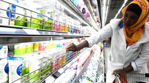 AFP A shop assistant wearing an orange headscarf and a white coat fills the shelves with dairy products at supermarket in Nairobi, Kenya